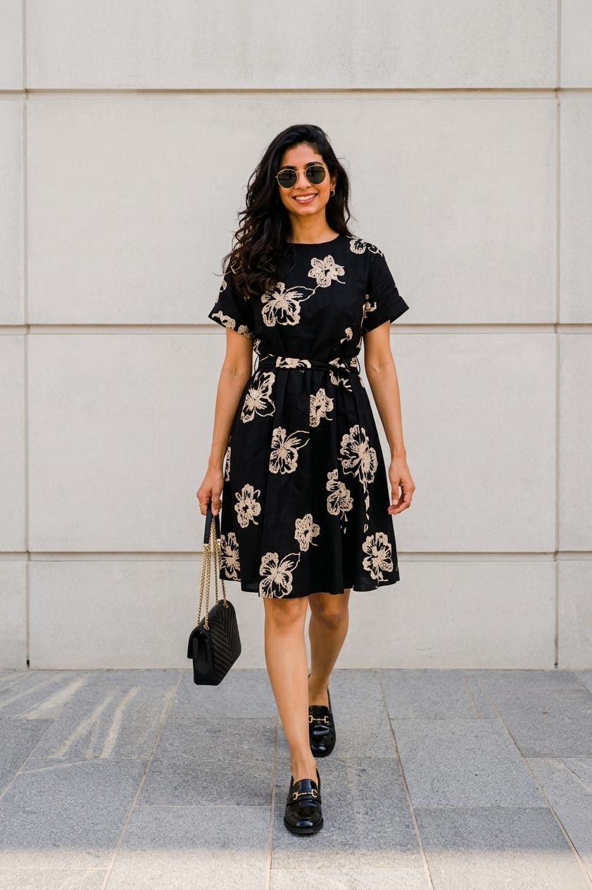 Woman wearing a black floral dress against a light gray wall.